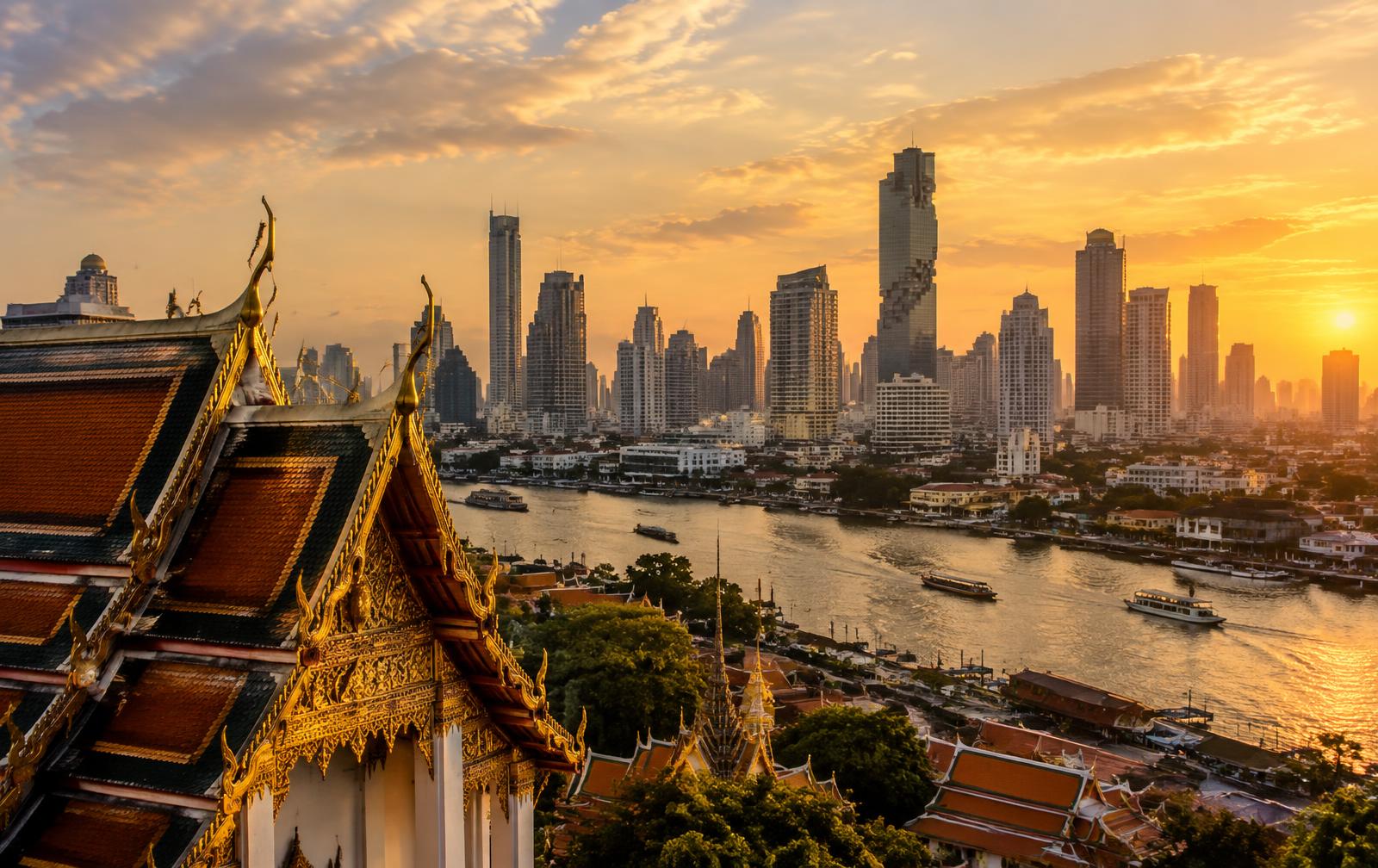 Bangkok skyline and a gilded temple roof above the Chao Phraya river at sunset